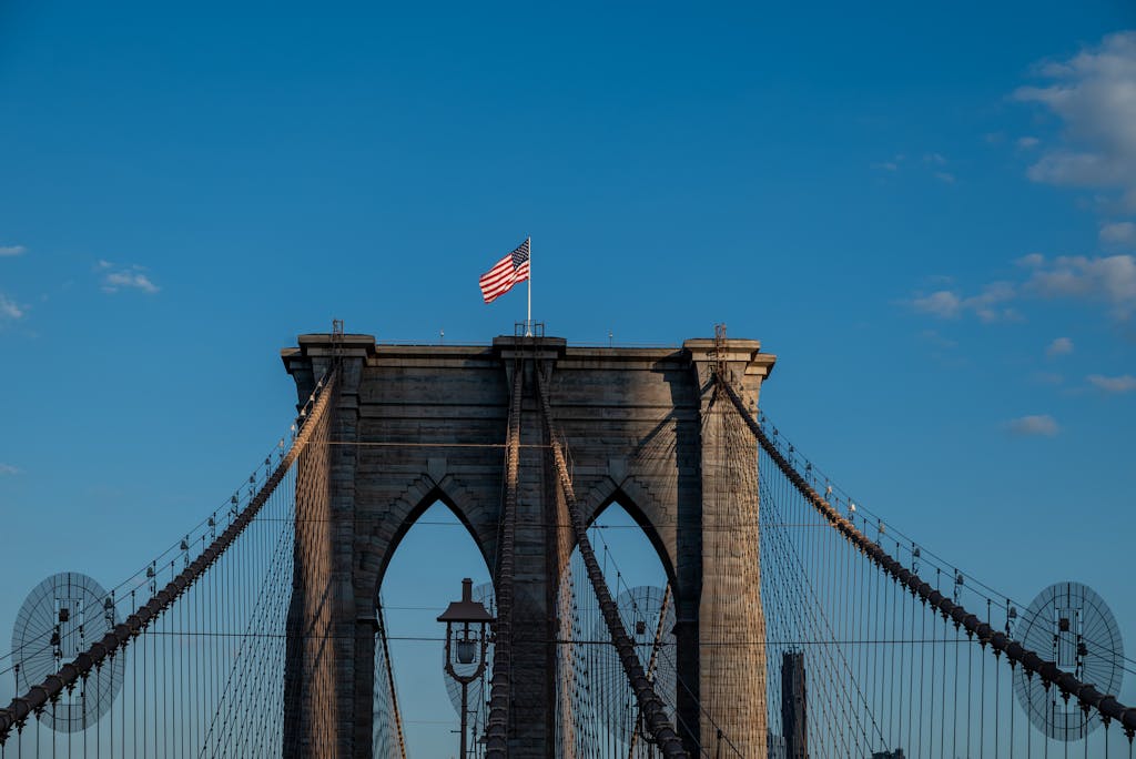 A stunning view of the Brooklyn Bridge under a clear blue sky, showcasing the iconic American flag atop.
